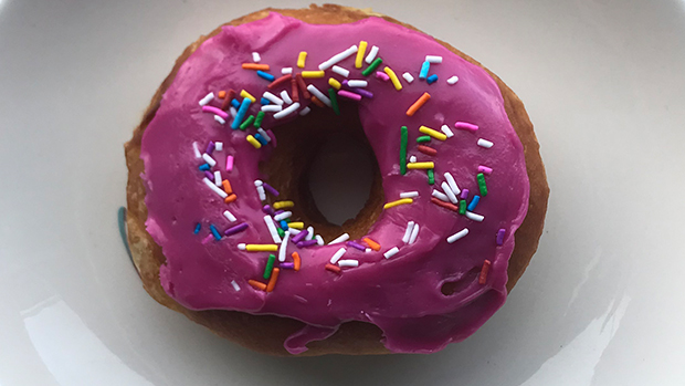 A pink doughnut with sprinkles sits on a white plate.