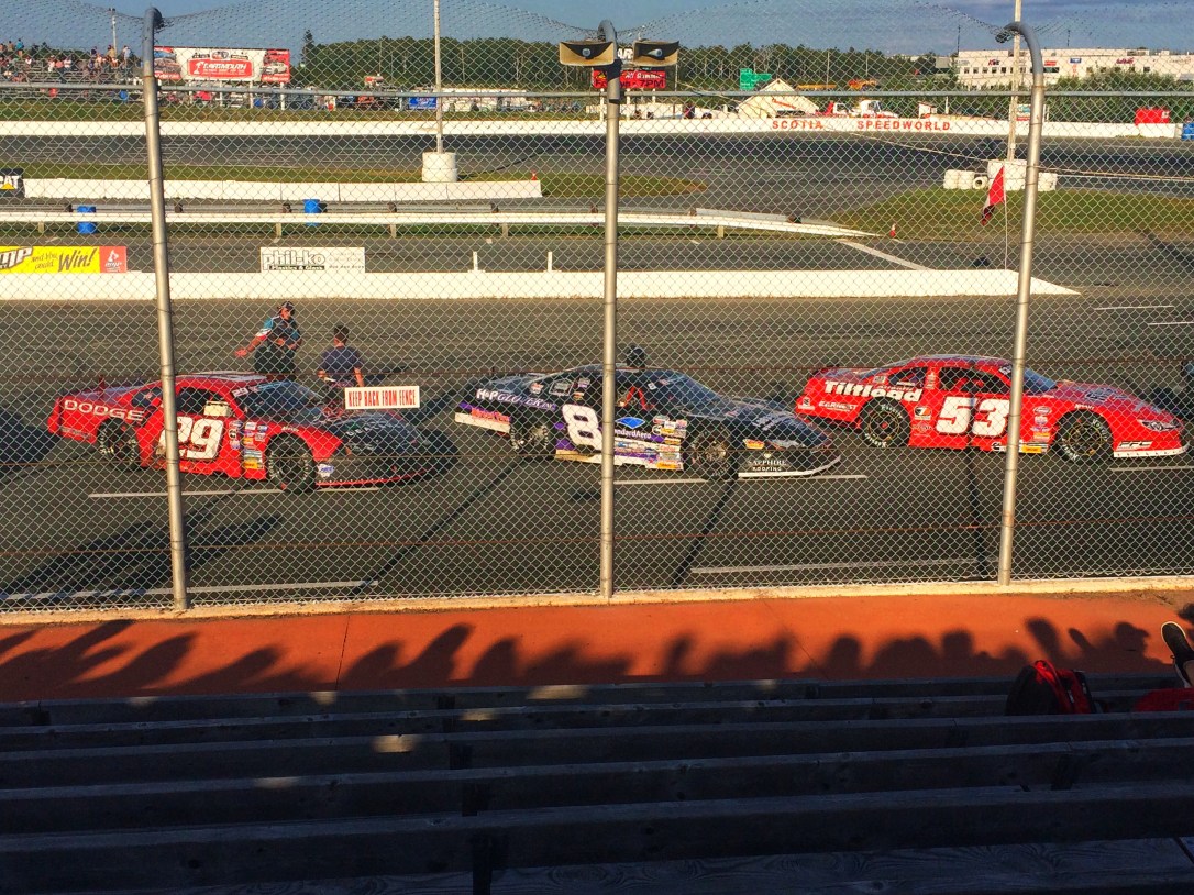 Three race cars are lined up in front of a chain link fence at Scotia Speedworld.