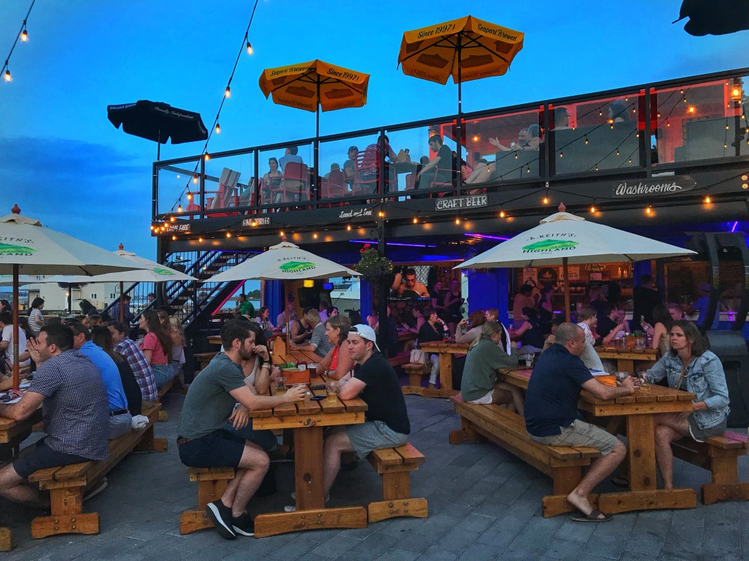People sit on picnic tables drinking beer at the Stubborn Goat Beer Garden on Halifax's boardwalk.
