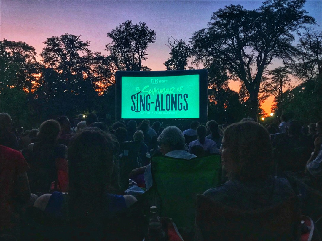 People are sitting on lawn chairs watching a movie outdoors.